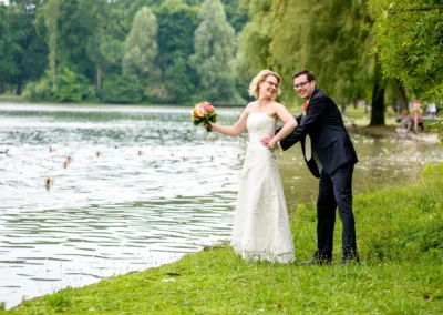 Brautpaar lacht neben Kleinhesseloher See im Englischen Garten Muenchen bei ihrer Hochzeitsreportage.