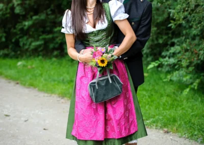 Paar in traditioneller Tracht, laechelnd in einem Park. Hochzeitsportraits in München, Hochzeitsfoto im Gruenen.