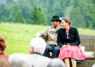 Brautpaar in traditioneller Tracht bei freier Trauung in Almbad-Sillberghaus, umgeben von gruenem Wald und Wiesen.