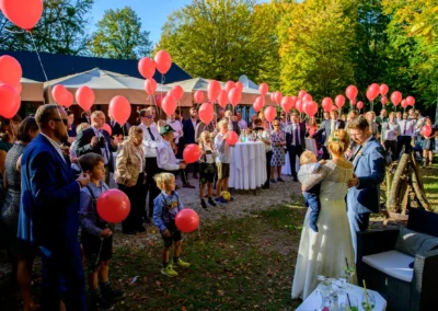 Hochzeitsgesellschaft mit roten Luftballons im Freien, Braut und Bräutigam mit Kind im Gruenwalder Forst.
