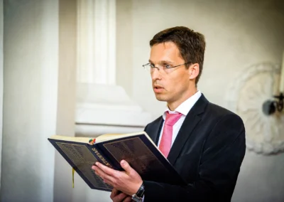 Mann mit Brille und rosa Krawatte liest aus einem Buch bei Hochzeitsreportage in Gmund am Tegernsee.