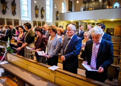 Gäste bei einer kirchlichen Trauung in München, aufmerksam das Hochzeitsprogramm lesend. Hochzeitsreportage.