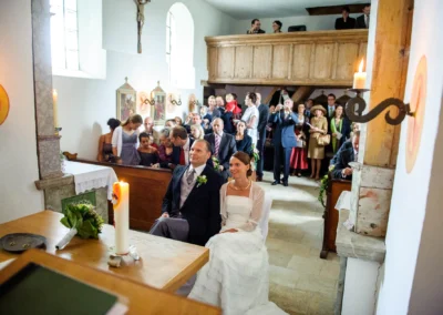Hochzeitsreportage in der Kirche, Brautpaar sitzt vor dem Altar, Gaeste stehen, bei Freising in Oberbayern.