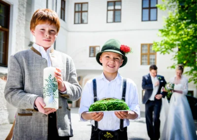 Zwei Kinder in traditioneller Tracht bei Hochzeit im Kloster Seeon tragen Kerze und Brot. Hochzeitsfotografie Oberbayern.