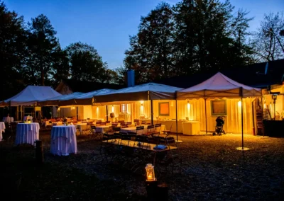 Abendliche Hochzeitslocation mit beleuchteten Zelten und Tischen im Waldhaus Alte Tram bei Muenchen, festlich geschmueckt.