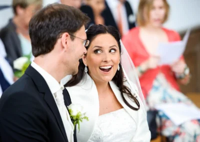 Brautpaar laechelt einander waehrend der kirchlichen Trauung in Aufkirchen am Starnberger See an. Hochzeitsfoto.