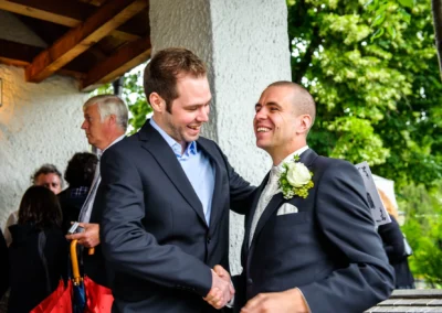 Zwei Männer in Anzug lachen bei einer kirchlichen Trauung in Murnau am Staffelsee. Hochzeitsfotograf Murnau.