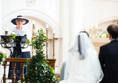 Eine Frau spricht bei einer kirchlichen Trauung. Brautpaar sitzt davor. Hochzeitsreportage Aufkirchen.