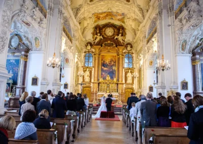Kirchliche Trauung im Kloster Benediktbeuern, Brautpaar am Altar, Gaeste auf Kirchenbaenken. Hochzeitsfotografie.