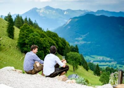Zwei Maenner in Lederhosen bei einer Hochzeit mit Blick auf die Berge nahe des Chiemsees. Hochzeitsfotografie