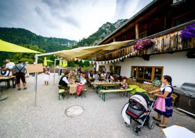 Hochzeitsfeier im Freien bei der Wuhrsteinalm Chiemgau mit Gaesten an Tischen, Bergen im Hintergrund.