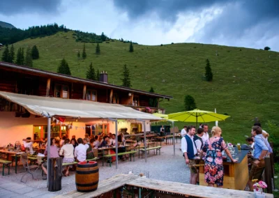 Gäste bei einer Hochzeit auf der Terrasse der Wuhrsteinalm im Chiemgau, festliche Abendstimmung, Hochzeitsfotografie.