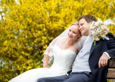Brautpaar bei Hochzeitsfotos am Tegernsee, Paar laechelt vor gelber Blumenwand. Hochzeitsfotografie in Bayern.