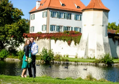 Paar bei Hochzeitsfotos im Schloss Blutenburg, Obermenzing, am Wasser mit historischer Architektur im Hintergrund.