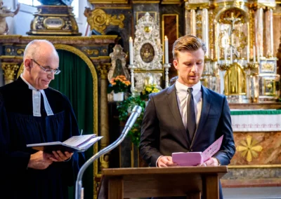 Pfarrer und Mann in Anzug vor Altar in Kirche nahe Tegernsee während der Trauung. Hochzeitsfotografie von kirchlicher Zeremonie.