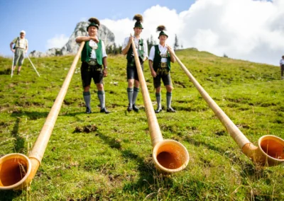 Männer in Tracht mit Alphörnern auf grüner Wiese nahe Kampenwand, festliche Hochzeit.