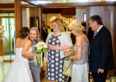 Braut umarmt Gast mit Blumenstrauss bei Hochzeit am Eibsee. Feiern in lockerer Atmosphaere, festgehalten in Hochzeitsfoto.