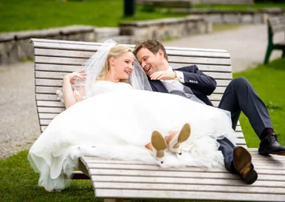 Brautpaar auf Holzbank am Tegernsee bei ihrer Hochzeit fotografiert. Natuerliche Hochzeitsfotos mit Freude und Liebe.