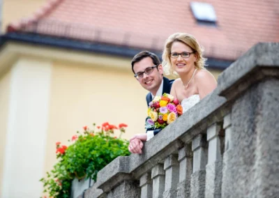 Brautpaar laechelt bei einer Hochzeit in Muenchen Schwabing, mit Blumenstrauss auf einer Terrassenbalkon. Hochzeitsfoto.