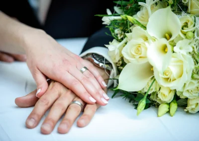 Verschraenkte Haende mit Eheringen und Blumenstrauss bei Hochzeit in Muenchen Schwabing, Hochzeitsfotografie.