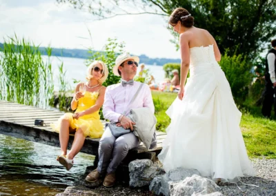 Braut in weissem Kleid mit Gästen am Seeufer bei einer Hochzeitsfeier am Starnberger See. Hochzeitsfotografie.
