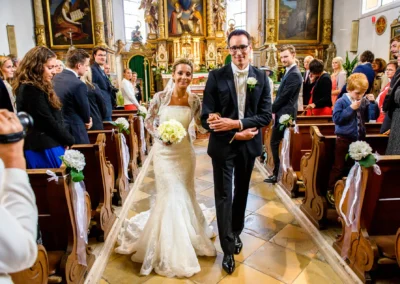 Brautpaar bei kirchlicher Trauung in Waakirchen, begleitet von Gästen, schrittweise zum Altar. Hochzeitsfotografie.