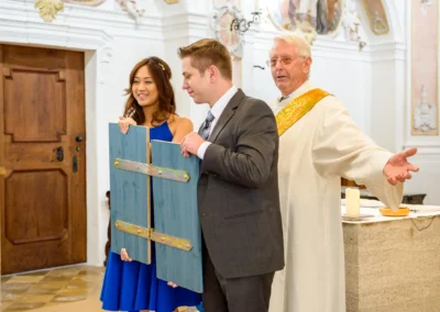 Drei Personen bei kirchlicher Trauung in Fischbachau, Brautpaar mit Priester während einer Hochzeitsreportage.