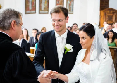 Bräutigam und Braut bei kirchlicher Trauung in Aufkirchen, Hochzeitsfotografie mit Pfarrer im Hintergrund.