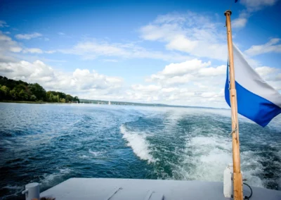 Bootsfahrt bei einer Hochzeit am Starnberger See, Sicht auf eine Flagge, Wasser und blauer Himmel. Hochzeitsfotograf.