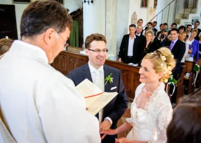 Brautpaar bei kirchlicher Trauung, Hochzeitsfotografie im Kloster Seeon, festlich geschmueckte Kirche, Gaeste im Hintergrund.