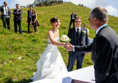 Brautpaar beim Handshake mit Standesbeamten auf Wiese bei Hochzeit, Kampenwand, Hochzeitsfotograf Oberbayern.