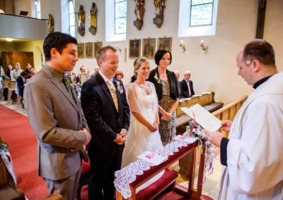 Kirchliche Trauung in Pasing: Brautpaar und Gaeste vor dem Altar mit Priester bei einer Hochzeitsreportage.