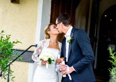 Brautpaar beim Kuss nach kirchlicher Trauung nahe Tegernsee, festgehalten in einer Hochzeitsfotografie.