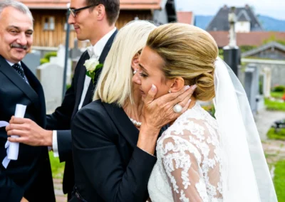 Braut umarmt Frau bei Hochzeit nahe Tegernsee, emotionale Momente festgehalten von Hochzeitsfotograf, Brautkleid detailliert