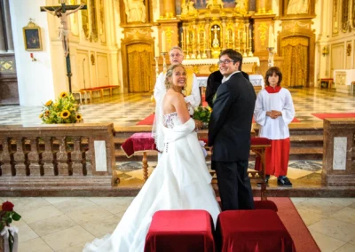 Brautpaar bei kirchlicher Trauung im Kloster Benediktbeuern, lächelnd am Altar, Hochzeitsfotografien aus Bad Tölz.