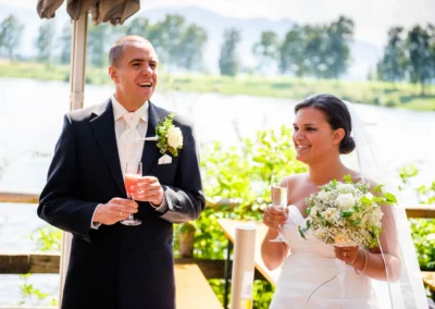 Brautpaar bei Hochzeitsfeier am Staffelsee, fröhlich mit Sektgläsern. Hochzeitsfotografie in Uffing am Staffelsee.