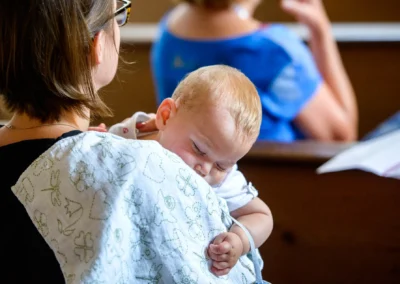 Frau haelt schlafendes Baby auf dem Arm waehrend kirchlicher Trauung in Taufkirchen bei Muenchen. Hochzeitsfoto.