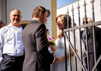 Brautpaar laechelnd vor Kirche in Muenchen, Hochzeitstrauung mit Gaesten daneben, festlich und froehlich.