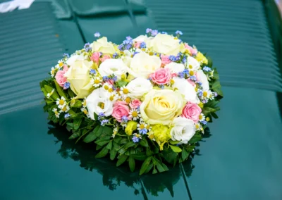 Blumenstrauss mit Rosen und Gänseblümchen auf grünem Autodach bei einer Hochzeit am Tegernsee fotografiert.