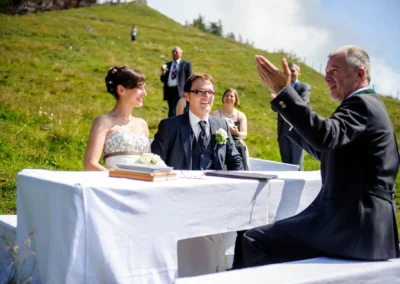 Brautpaar und Trauung im Freien bei Hochzeit in den Bergen nahe Chiemsee, lacht während der Zeremonie.
