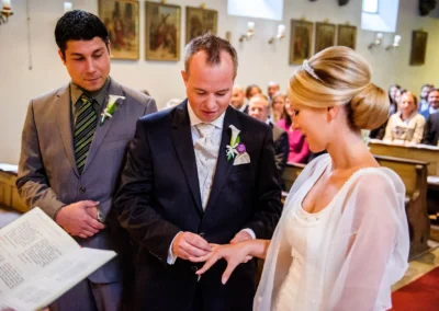 Brautpaar tauscht Ringe in Kirche bei Trauung in Muenchen, umgeben von Gaesten, festgehalten in Hochzeitsfoto.