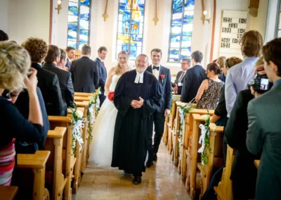 Pfarrer leitet kirchliche Trauung in Garmisch, Braut und Braeutigam laecheln, umgeben von Gaesten. Hochzeitsreportage.