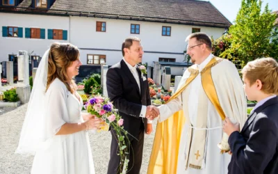 Brautpaar bei kirchlicher Trauung in Grosshadern mit Priester. Hochzeitsfoto in strahlendem Sonnenlicht.
