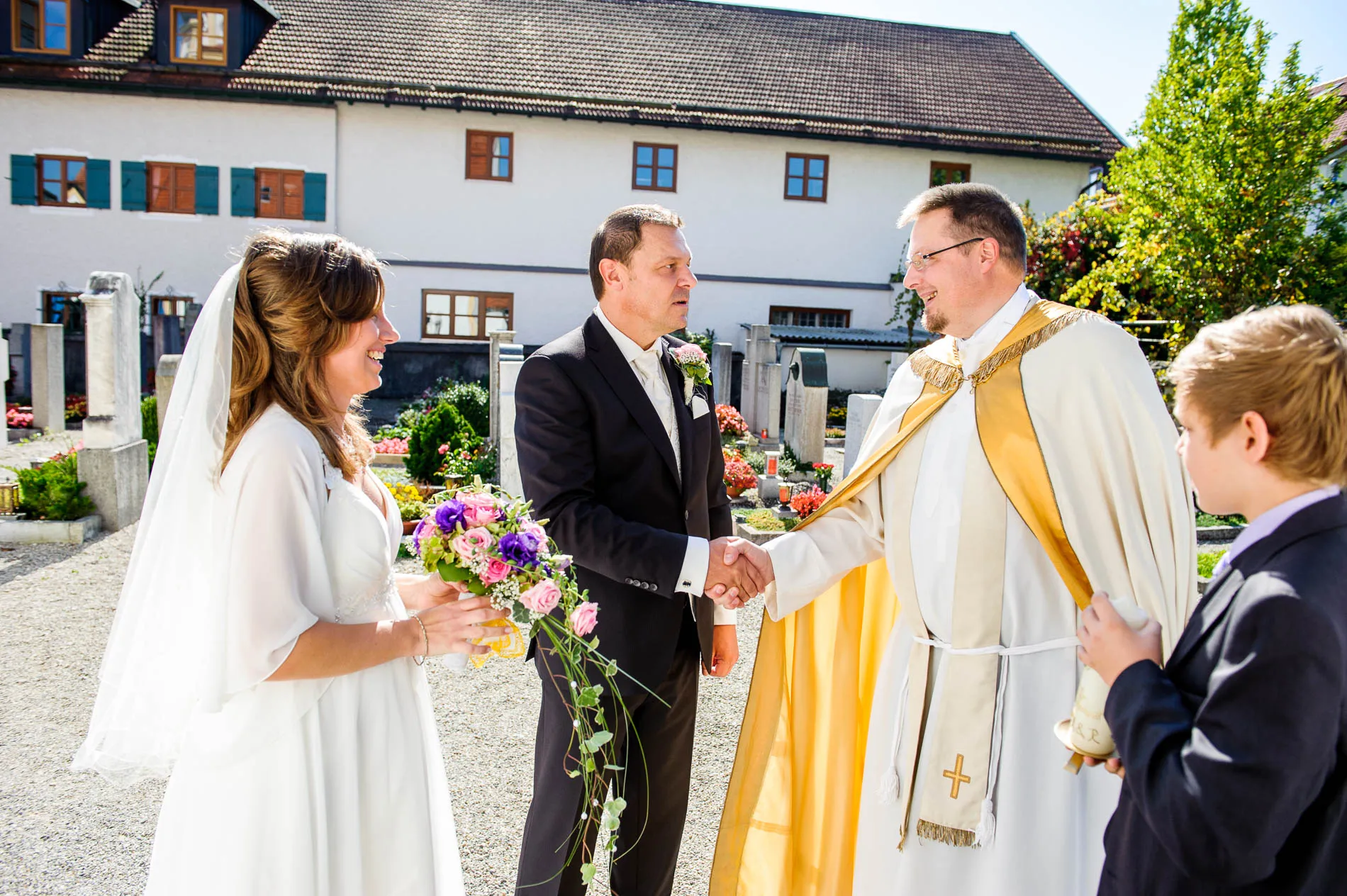 Brautpaar bei kirchlicher Trauung in Grosshadern mit Priester. Hochzeitsfoto in strahlendem Sonnenlicht.