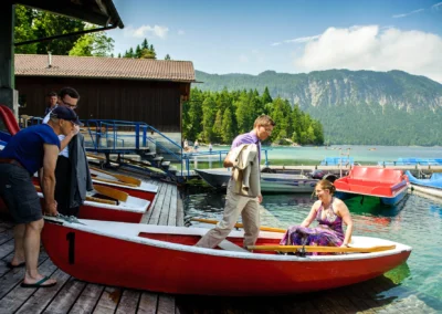 Ein Paar bei Hochzeitsreportage am Eibsee, steigt in ein Ruderboot. Entspannte Hochzeitsfotografie in malerischer Kulisse.
