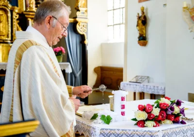 Priester segnet Kerzen bei kirchlicher Trauung in Taufkirchen, nahe Muenchen. Hochzeitsfotografie von Tischdekoration.