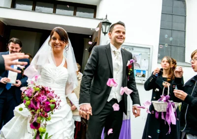 Brautpaar beim Verlassen der Kirche, romantische Hochzeitsreportage in St. Vitus Gilching mit Blumen und Seifenblasen.