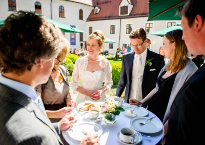 Gruppengeplauder bei Hochzeit im Kloster Seeon nahe Chiemsee. Brautpaar mit Gaesten im Freien bei Sonnenschein.