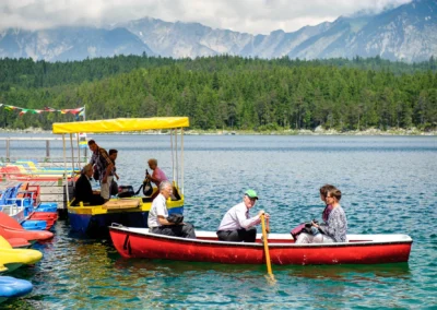 Menschen in Booten auf dem Eibsee bei einer Hochzeit; Hintergrund mit Bergen und Wald, perfekte Kulisse für Hochzeitsreportagen.