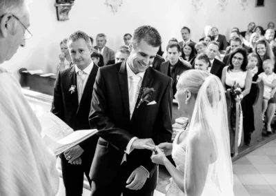 Brautpaar bei kirchlicher Trauung in Taufkirchen, Ringe werden ausgetauscht, umgeben von Gaesten, Hochzeitsfoto.